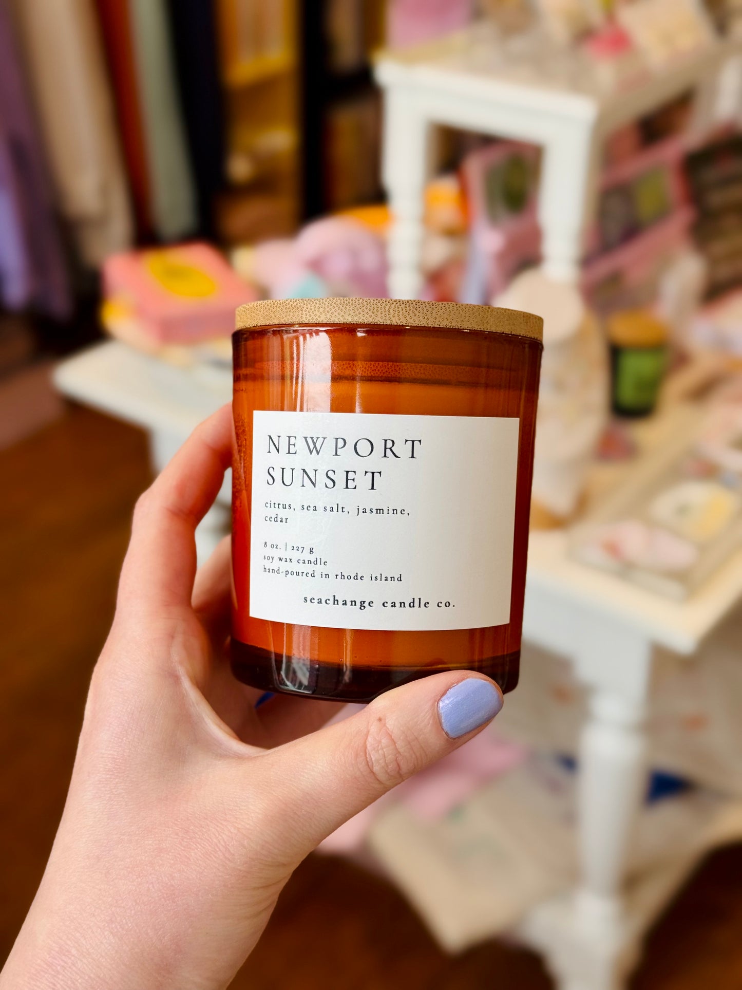 Hand holding a 'Newport Sunset' candle with a blurred indoor background