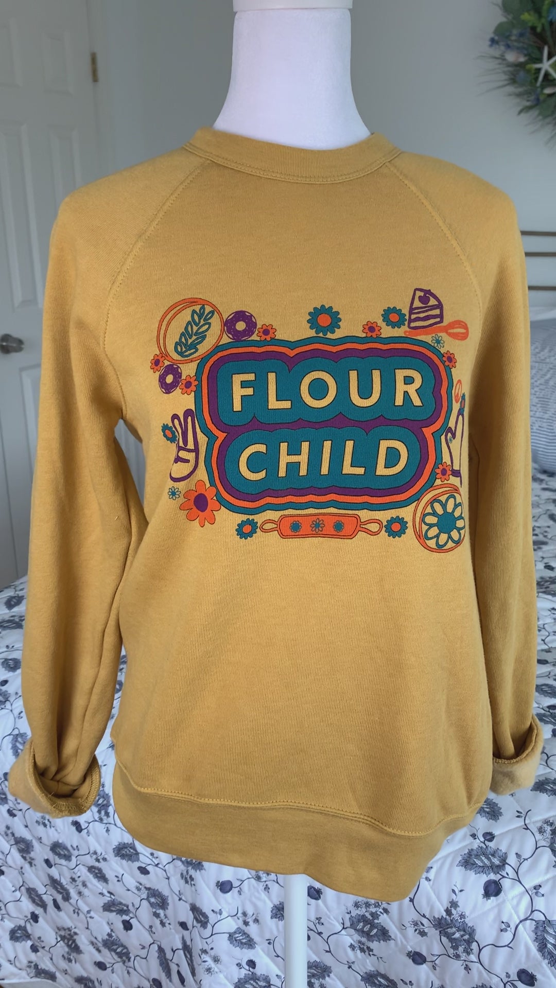 A yellow crewneck sweatshirt that reads "Flour Child" hangs on a manikin