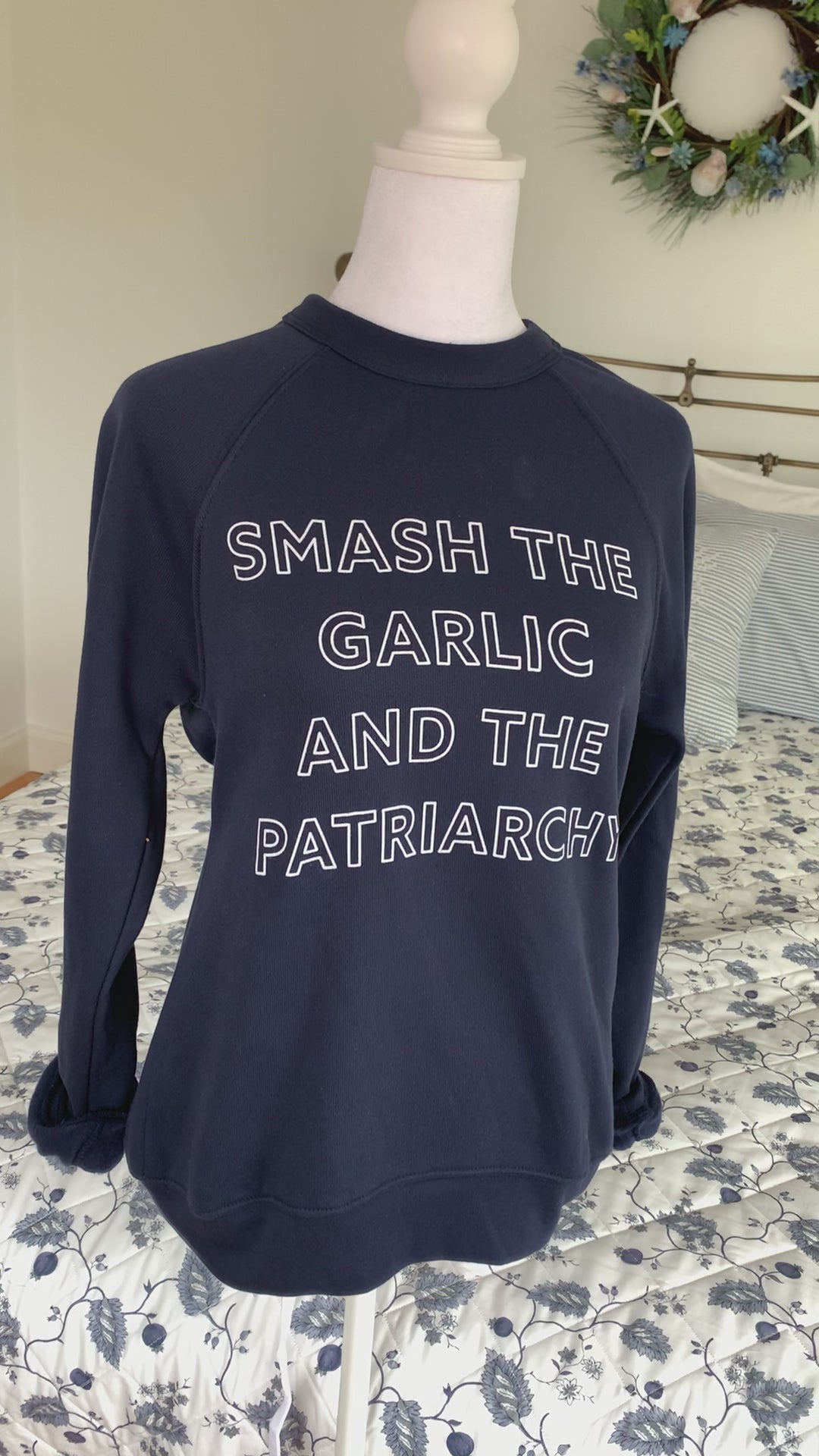 A navy blue crewneck that reads "Smash the Garlic and the Patriarchy" hangs on a manikin