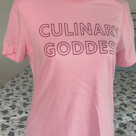 A light pink women's t-shirt that reads "Culinary Goddess" hangs on a manikin