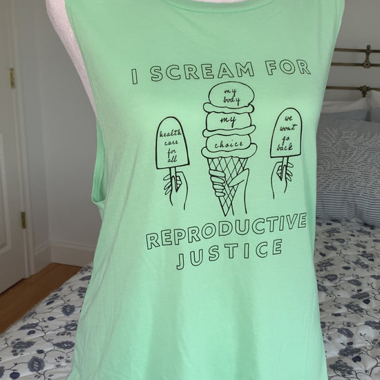 A mint green tank that reads "I scream for reproductive justice" hangs on a manikin 