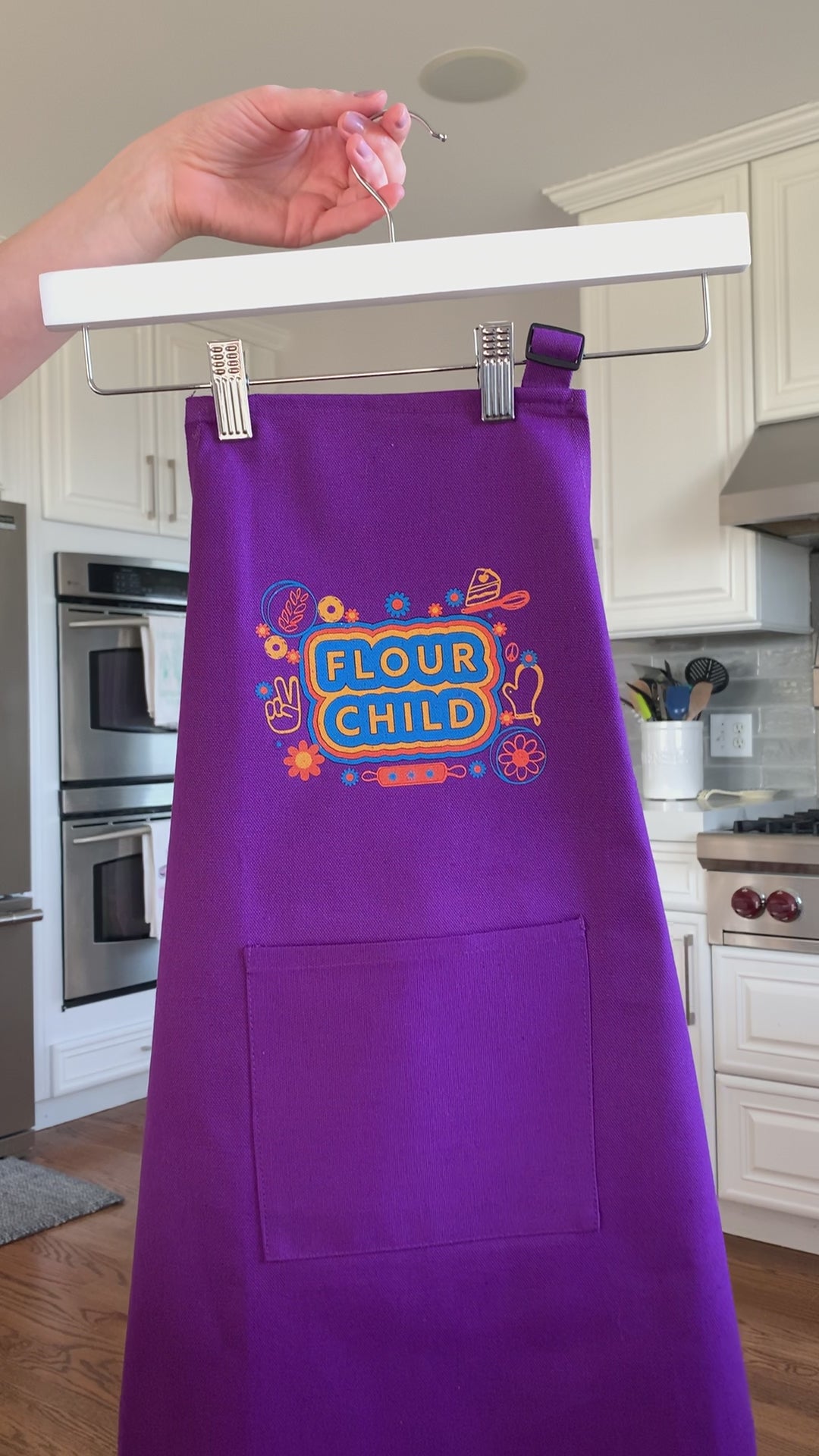 A purple kid's apron that reads "Flour Child" hangs on a hanger