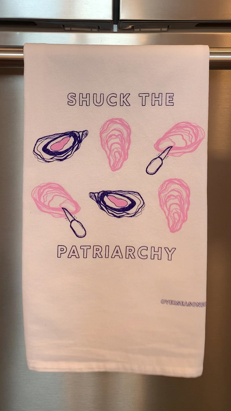 A white tea towel that reads "Shuck the Patriarchy" hangs in a kitchen