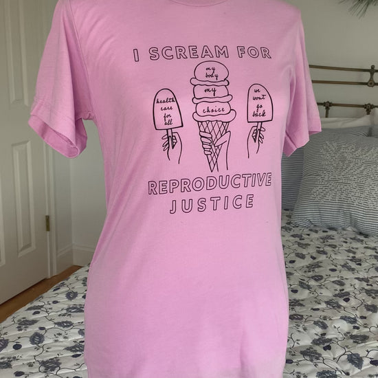 A lilac t-shirt that reads "I scream for reproductive justice" hangs on a manikin