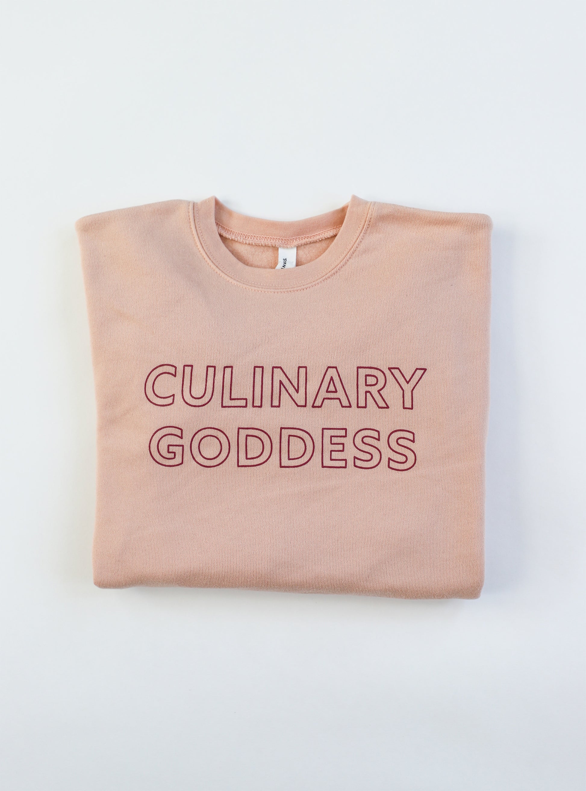 Folded pink crewneck sweatshirt with the words "Culinary Goddess"