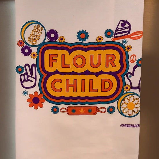 A white tea towel with the words "Flour Child" and colorful designs hangs in a kitchen
