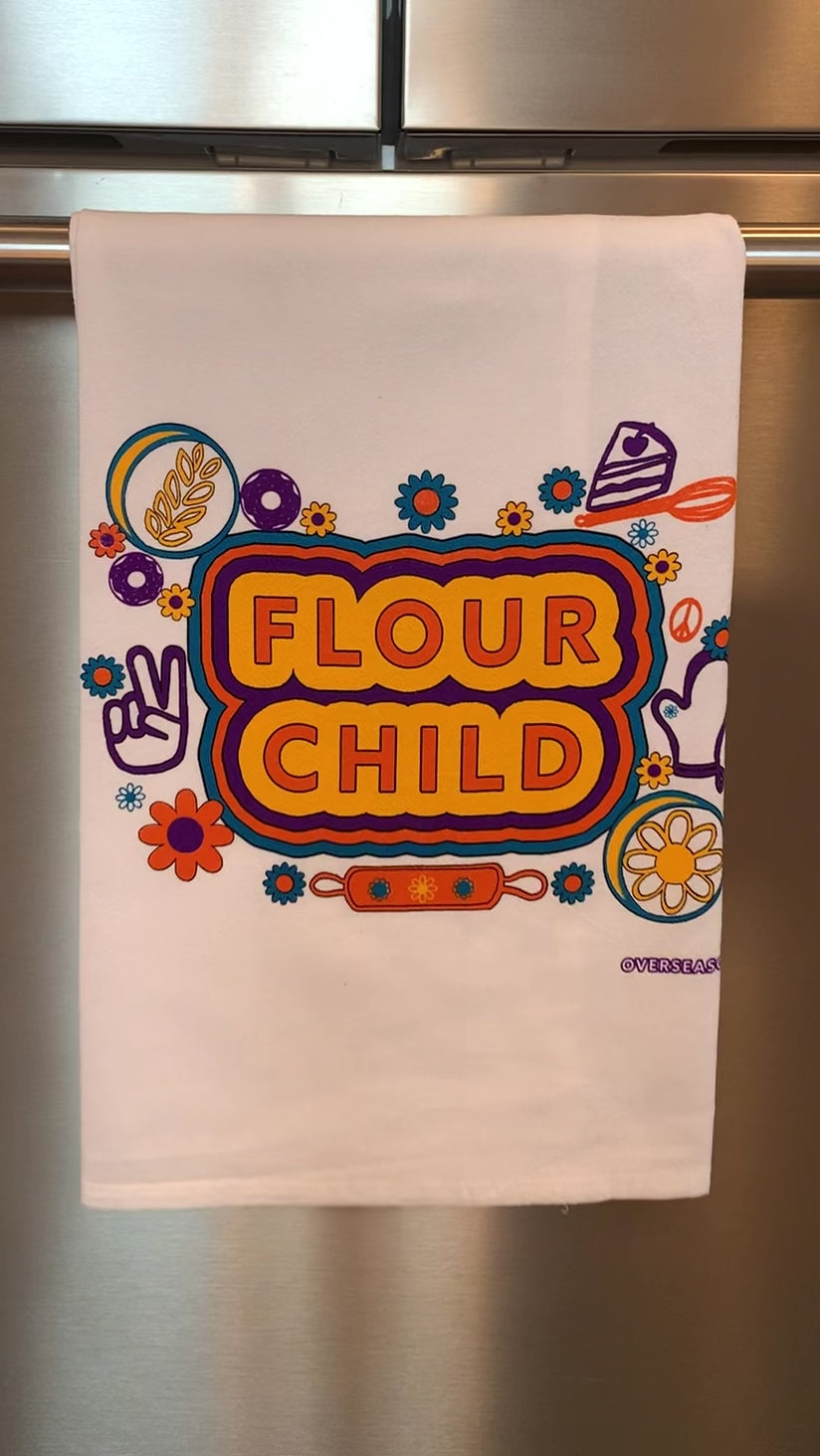 A white tea towel with the words "Flour Child" and colorful designs hangs in a kitchen