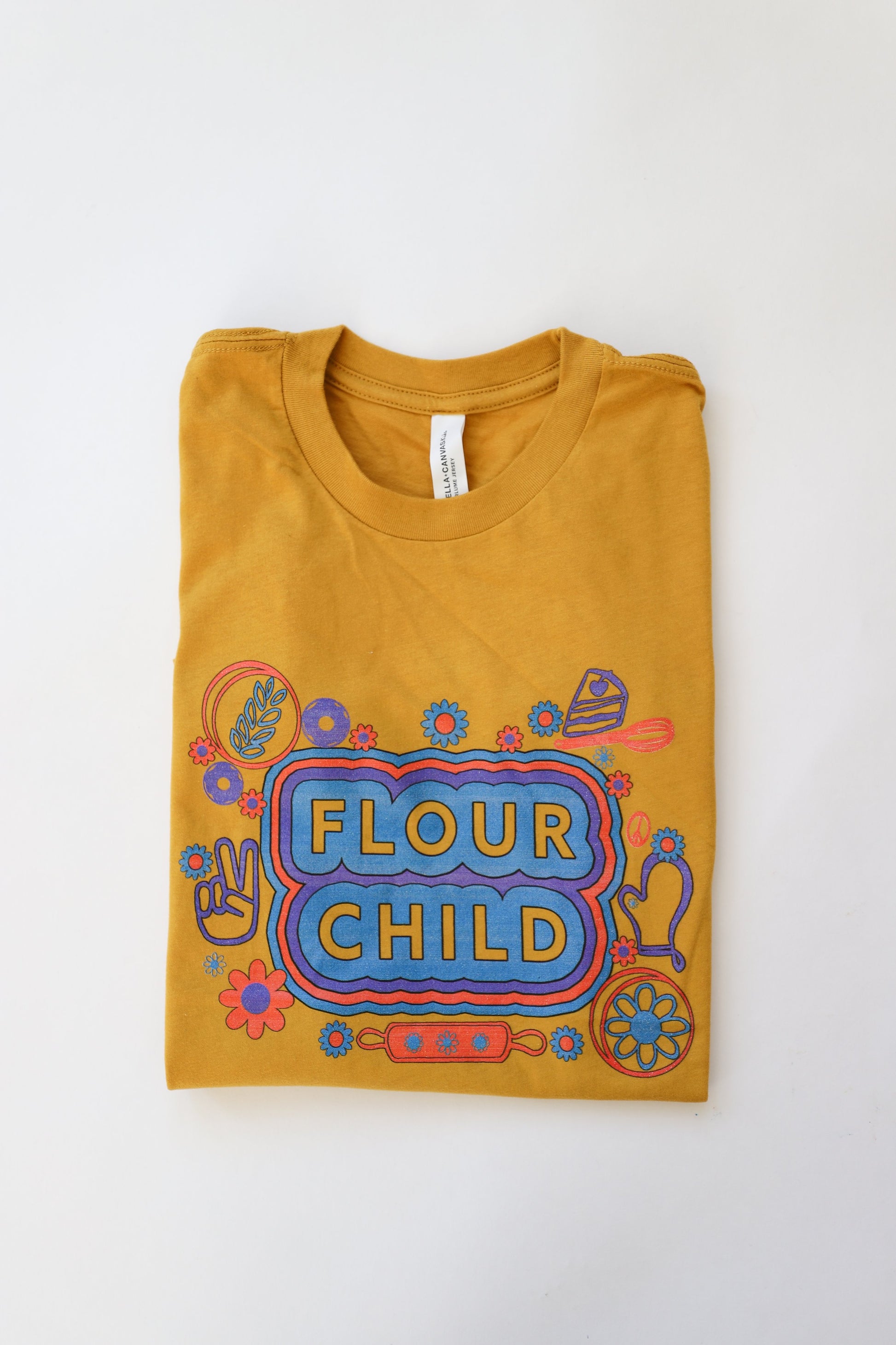 A folded yellow youth tee with the words Flour Child and fun kitchen illustrations