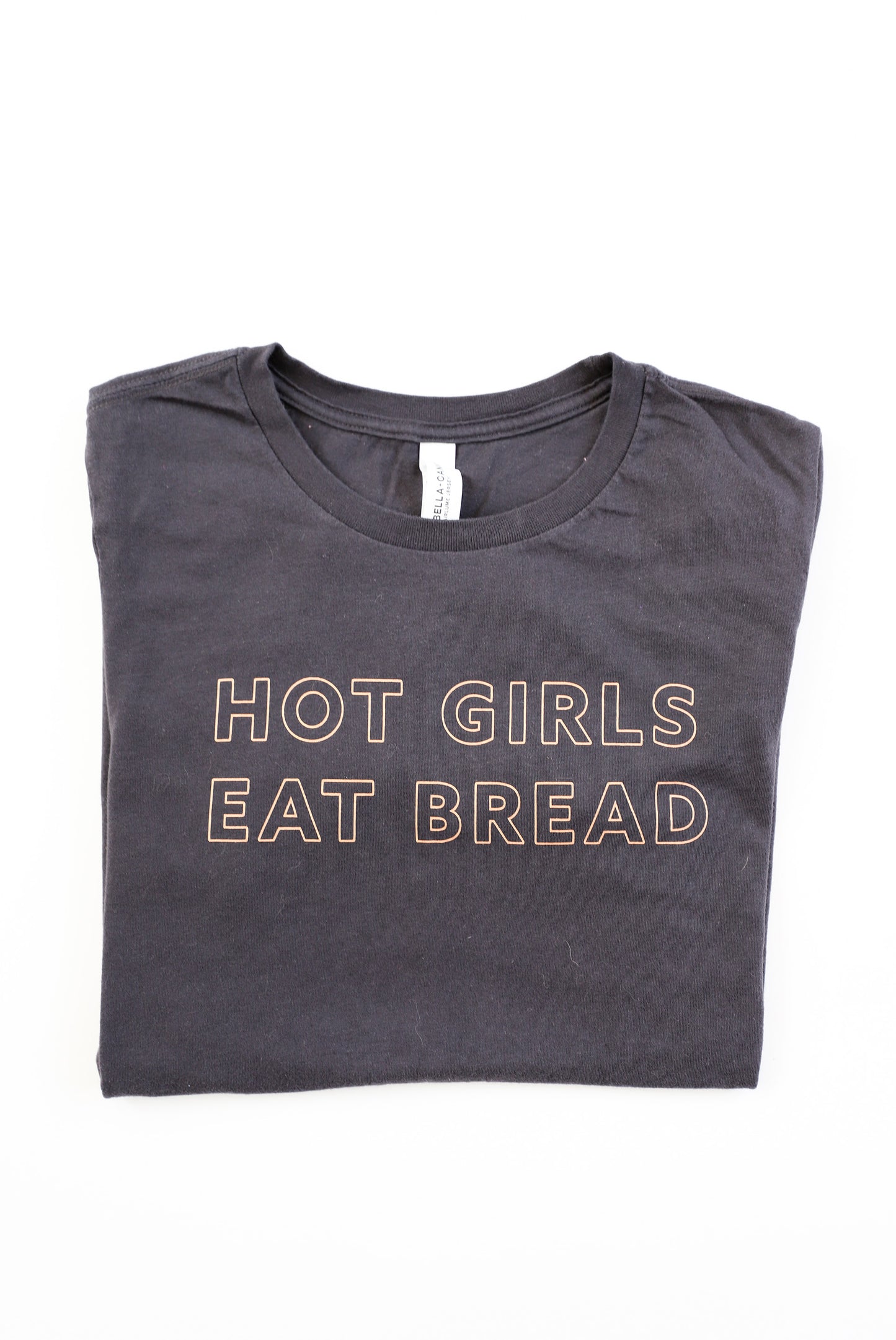 A folded dark grey t-shirt with the words Hot Girls Eat Bread and light pink letters