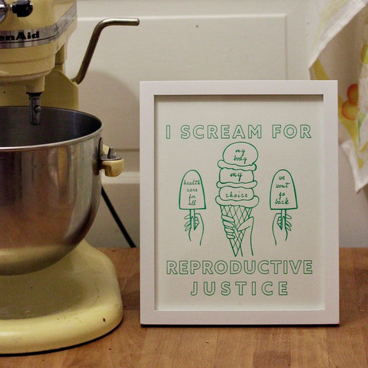 A print that reads "I Scream for Reproductive Justice" in mint green block letters with ice cream illustrations sits in a frame next to a mixer