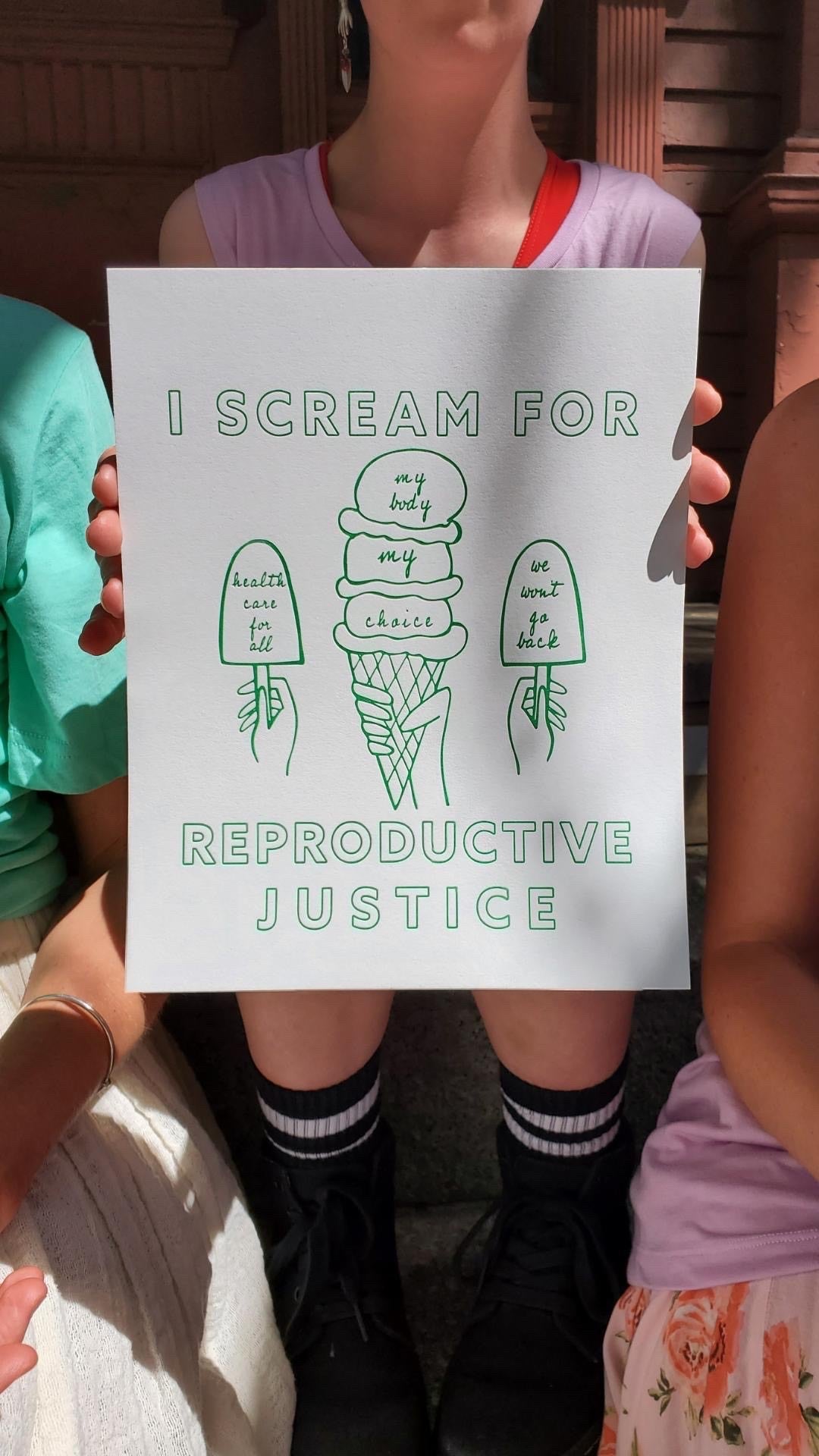 A woman holds up a print that reads "I Scream for Reproductive Justice"