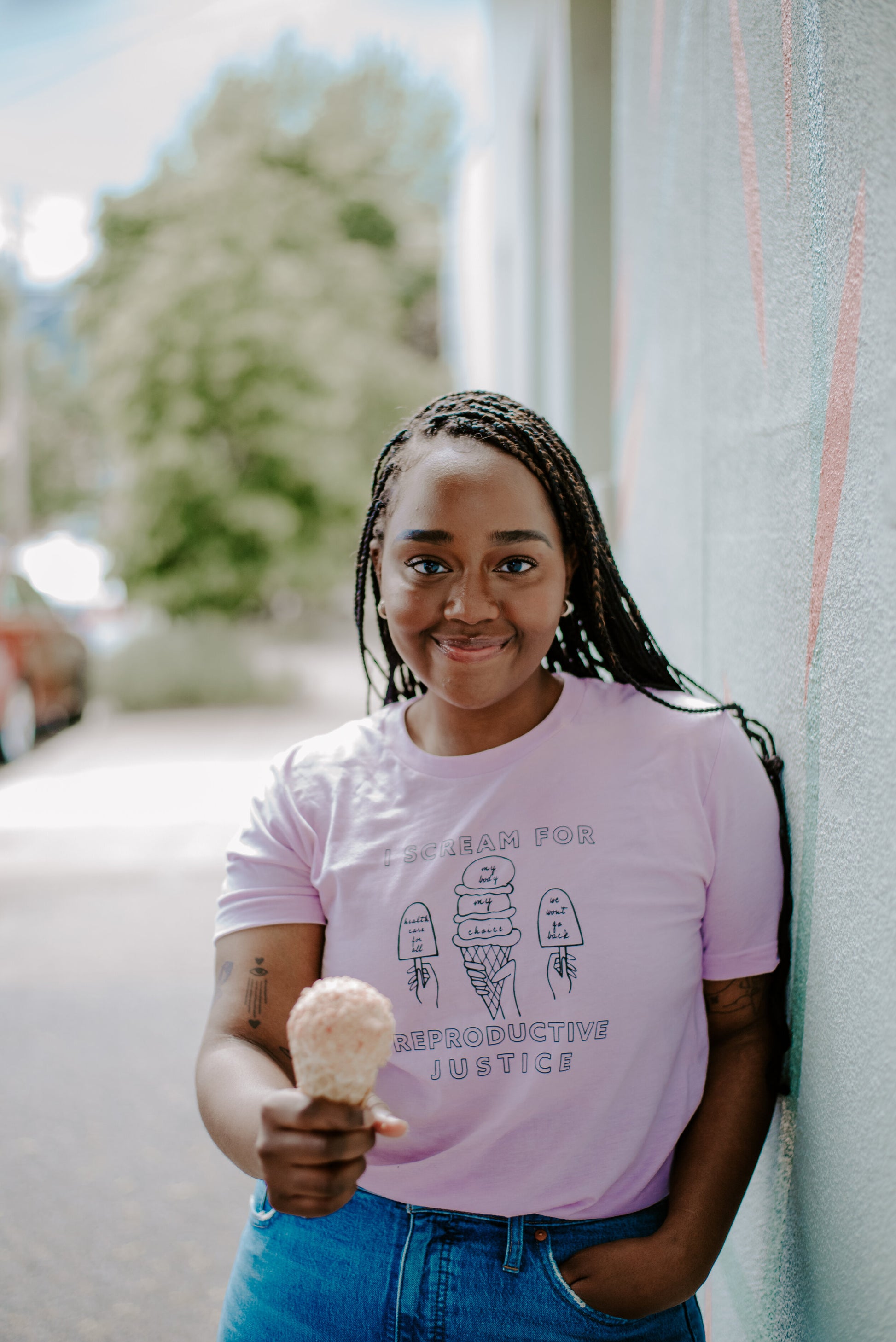 A woman wearing a lilac tee that reads "I Scream for Reproductive Justice" holds out an ice cream cone