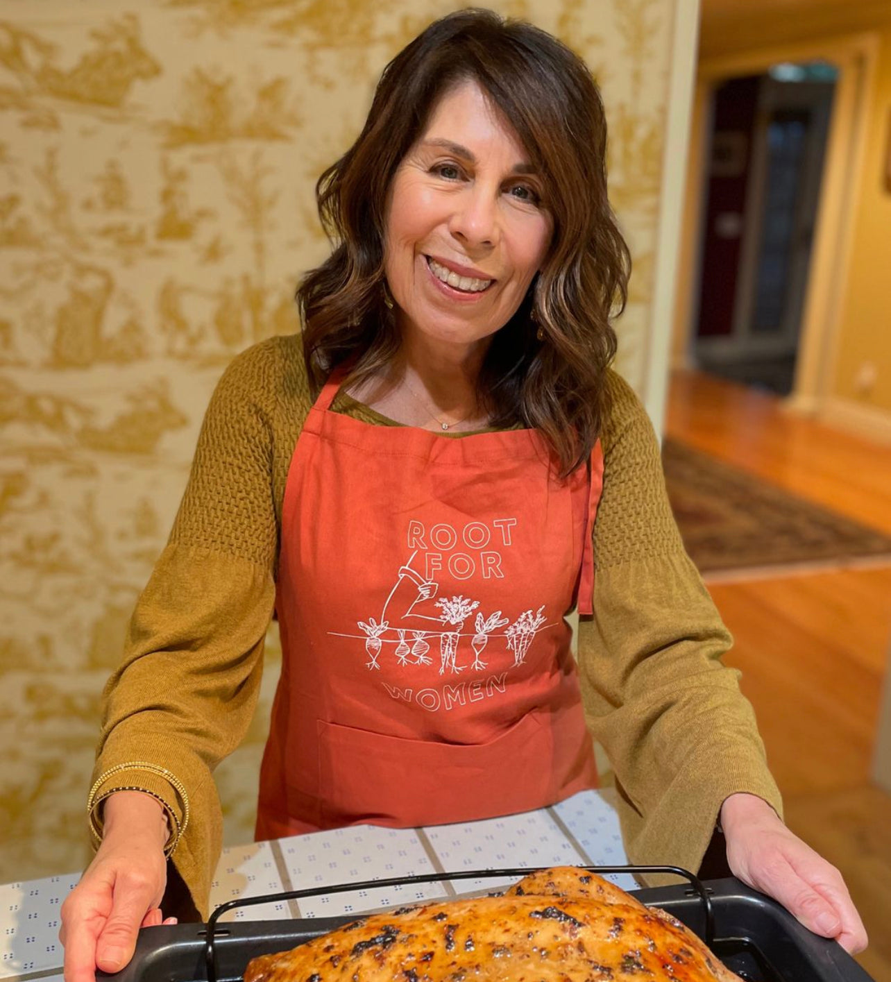 A woman wearing an orange "Root for Women" apron holds a turkey