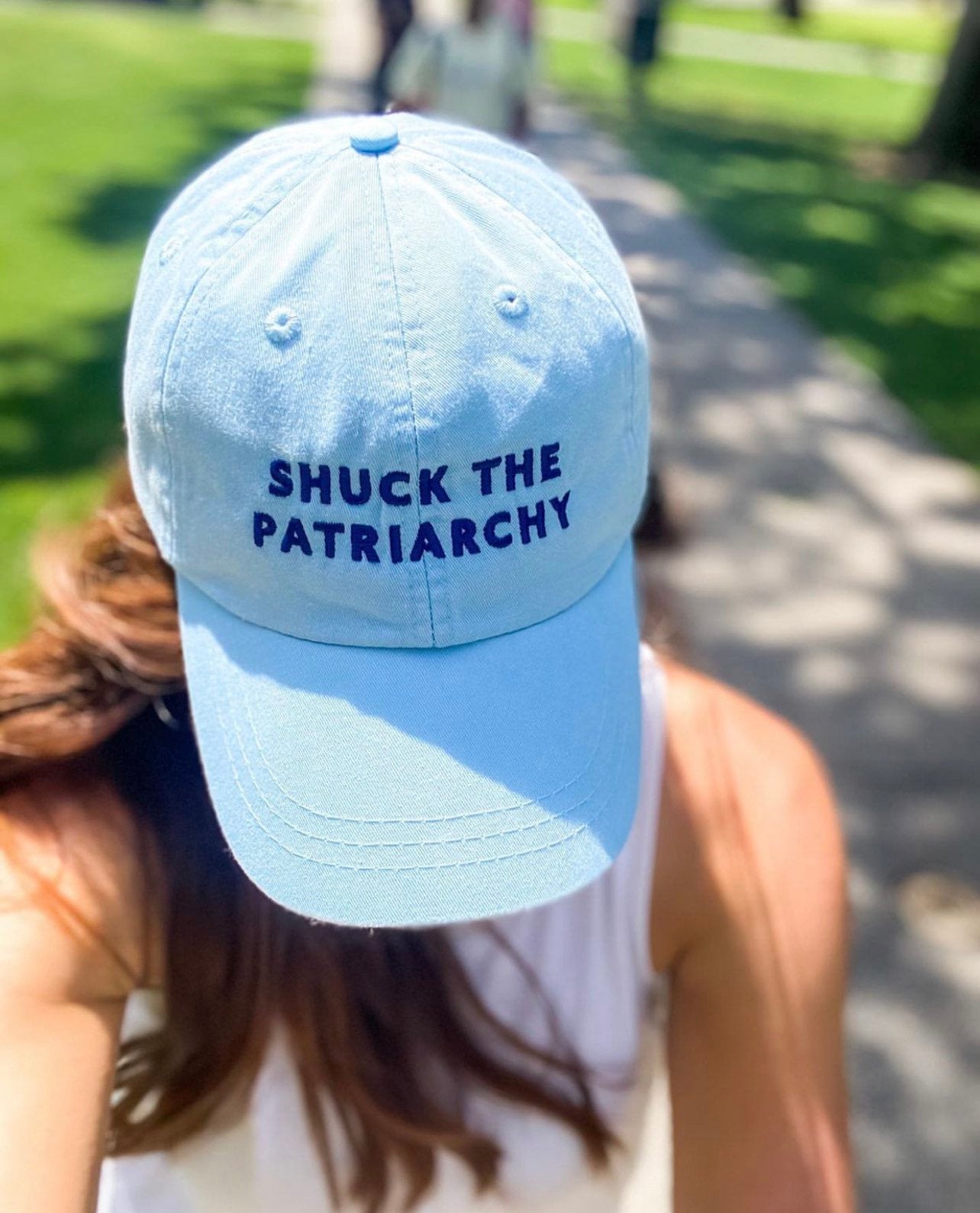 A woman wears a baseball cap that reads "Shuck the Patriarchy"