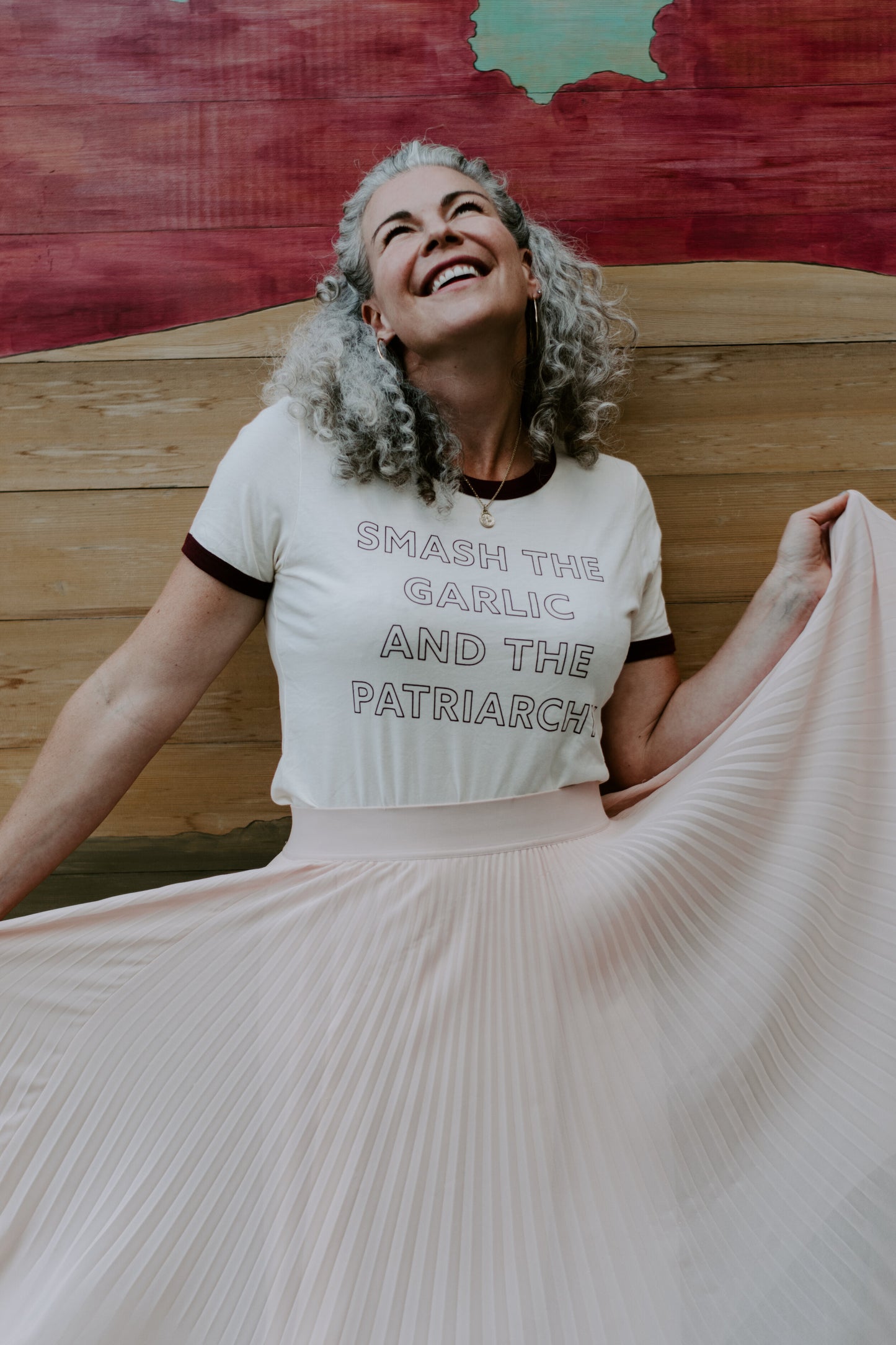A woman wears a "Smash the Garlic and the Patriarchy" ringer tee with a flowy pink skirt