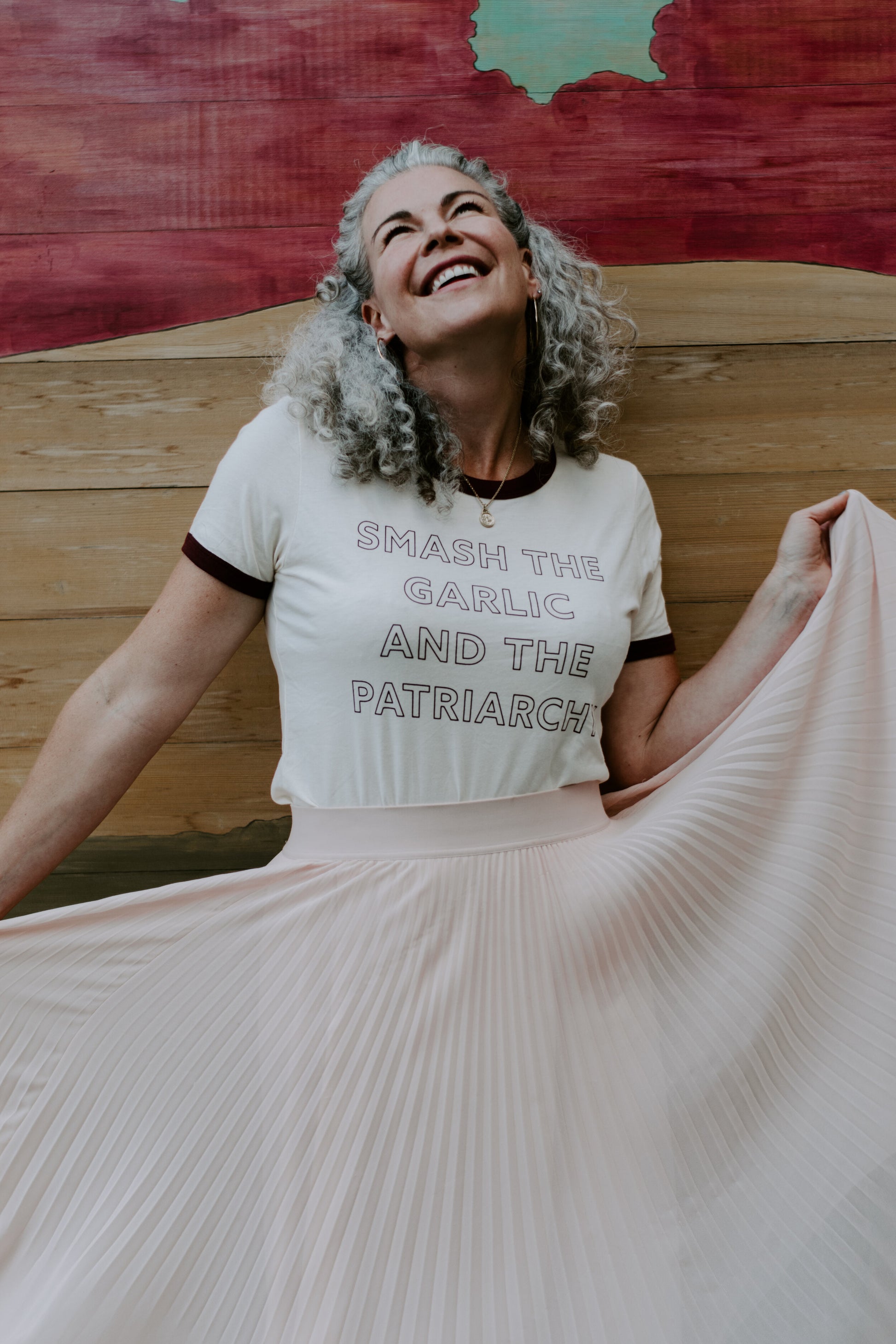 A woman wears a "Smash the Garlic and the Patriarchy" ringer tee with a flowy pink skirt