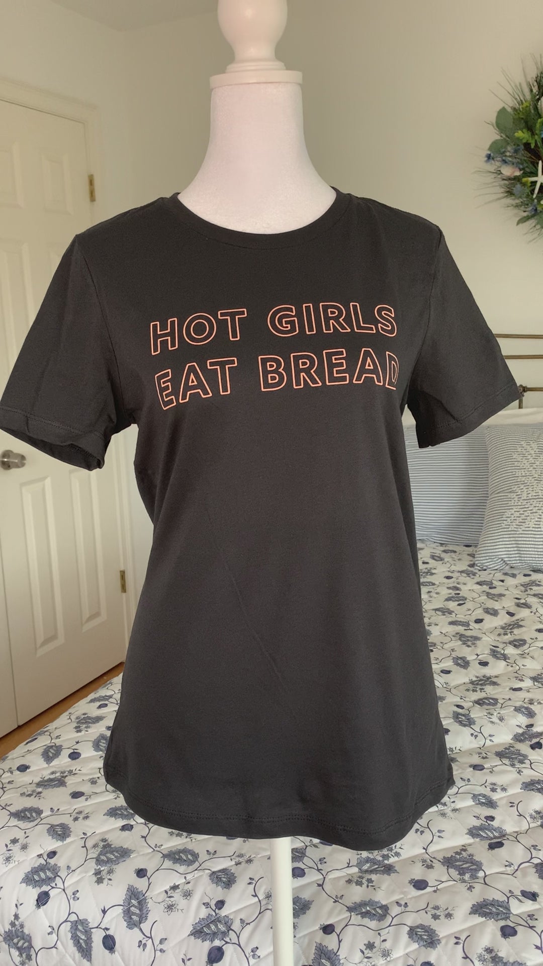 A dark grey tee that reads "Hot Girls Eat Bread" hangs on a manikin 