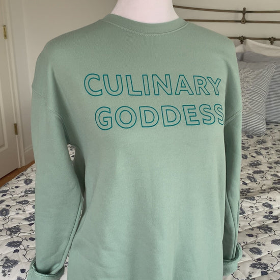 A dusty blue crewneck sweatshirt with the words "Culinary Goddess" hangs on a manikin