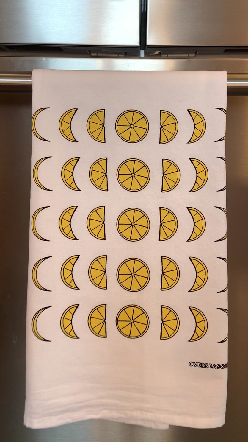 A white tea towel with lemon moon phases designs hangs in a kitchen