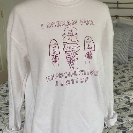 A white crewneck sweatshirt that reads "I scream for reproductive justice" hangs on a manikin