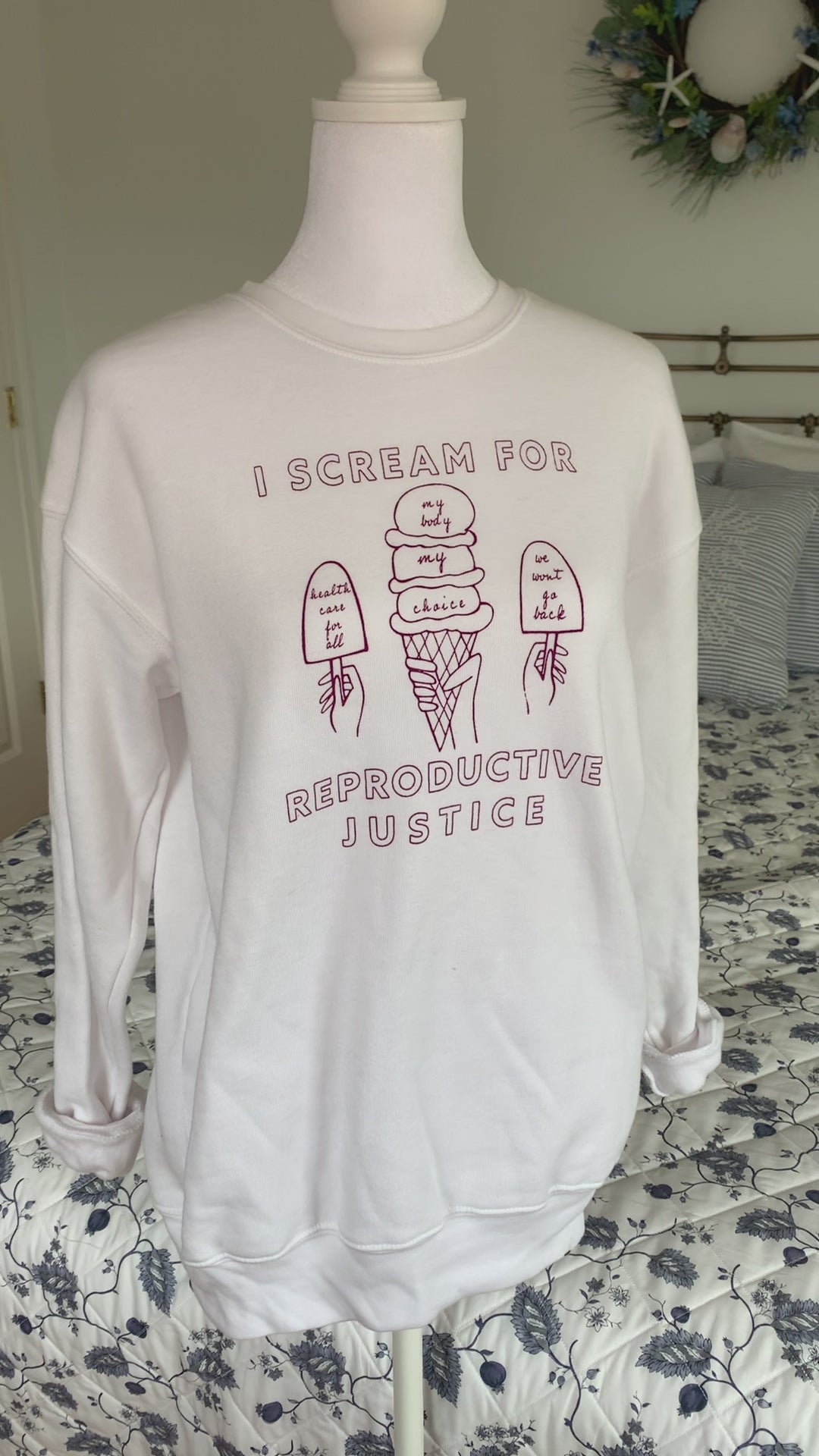 A white crewneck sweatshirt that reads "I scream for reproductive justice" hangs on a manikin