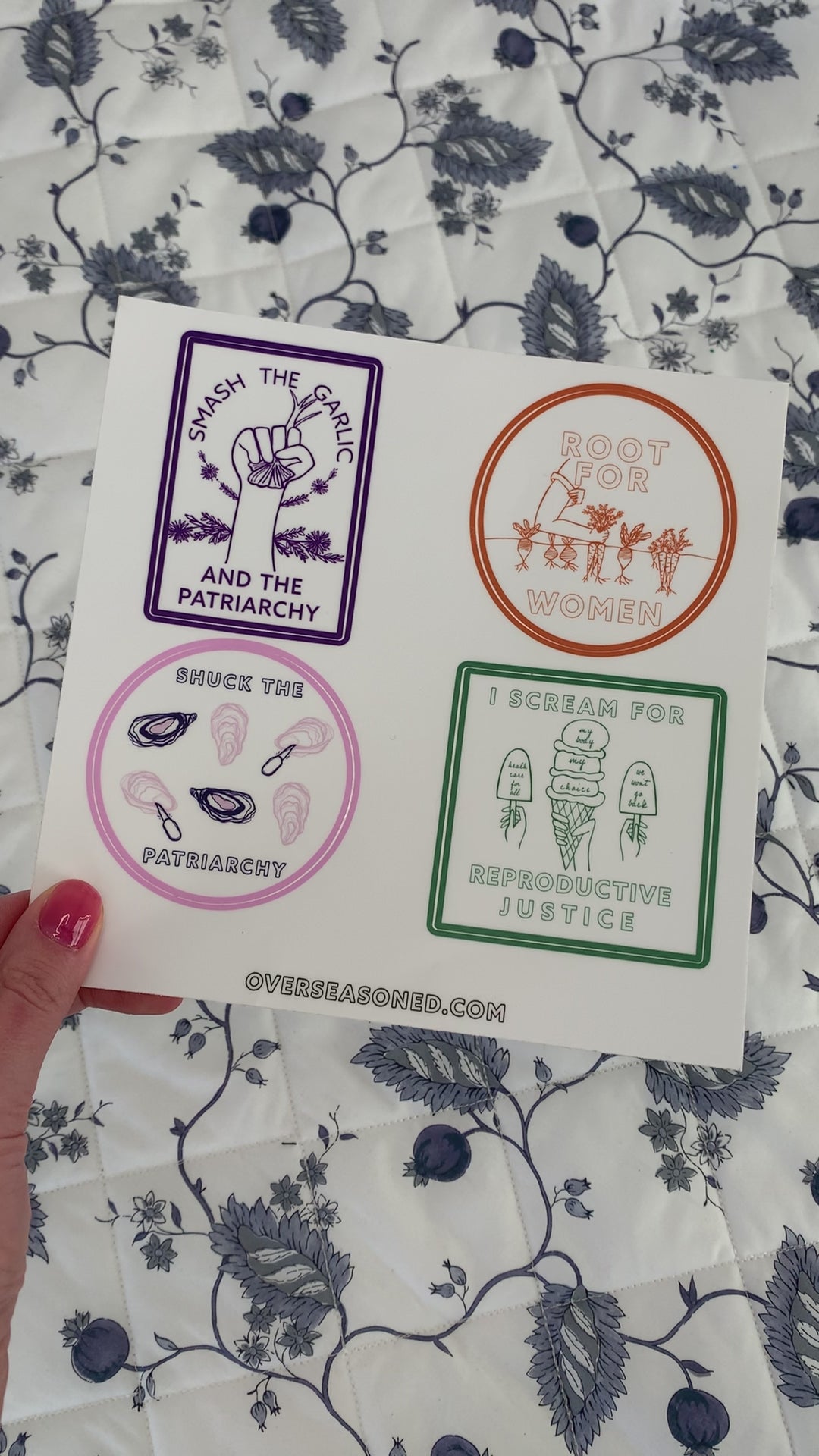A woman holds a sticker sheet with four sticker designs