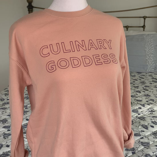 A light pink crewneck with the words "Culinary Goddess" hangs on a manikin