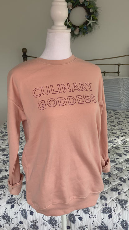A light pink crewneck with the words "Culinary Goddess" hangs on a manikin