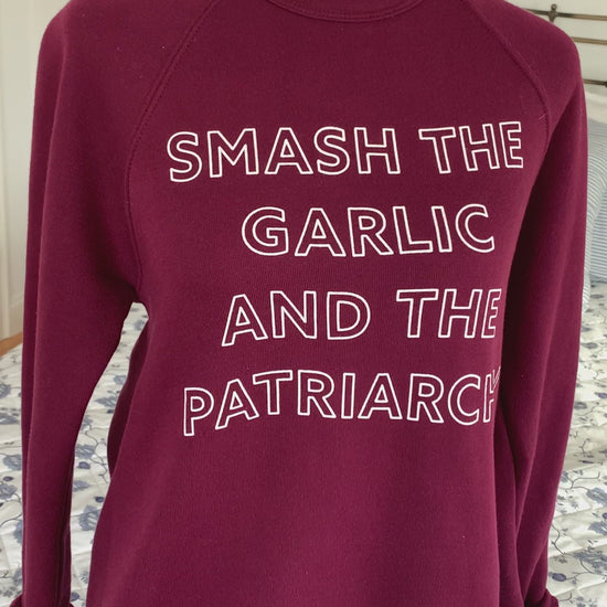 A maroon crewneck that reads "Smash the Garlic and the Patriarchy" hangs on a manikin