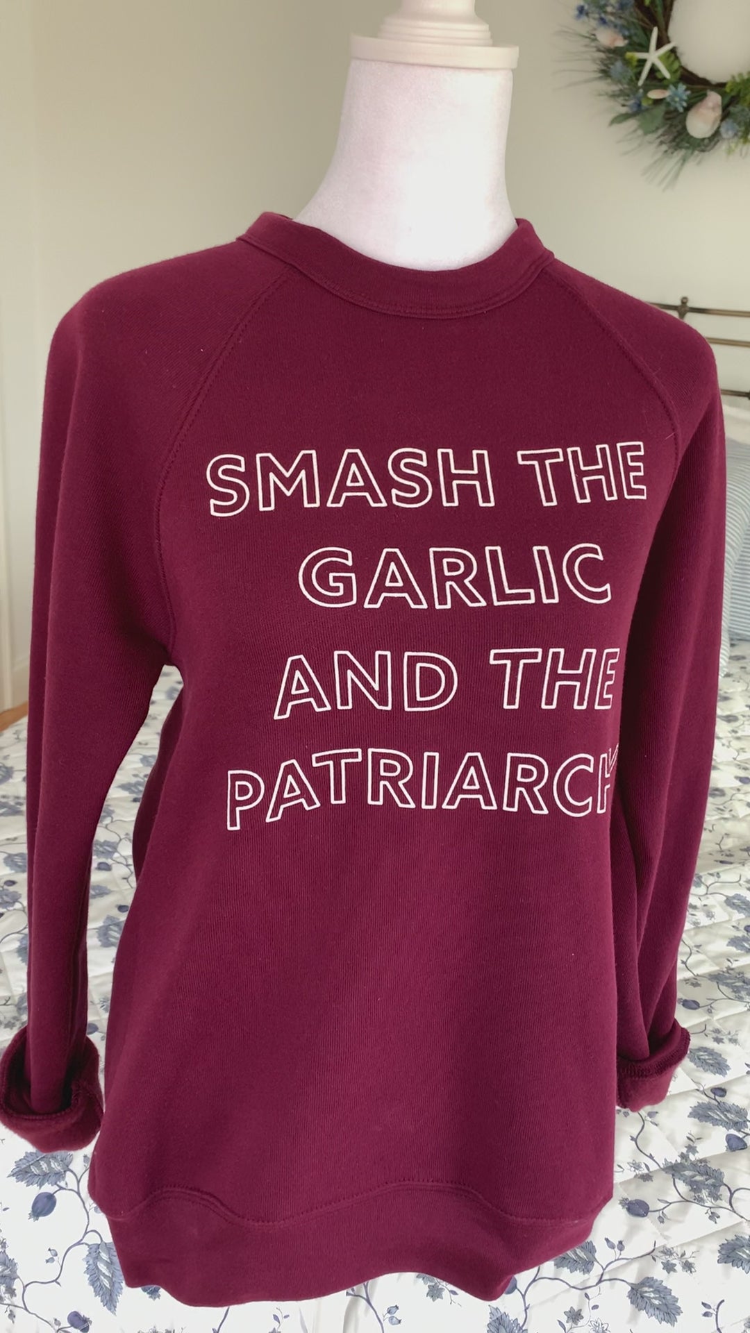 A maroon crewneck that reads "Smash the Garlic and the Patriarchy" hangs on a manikin