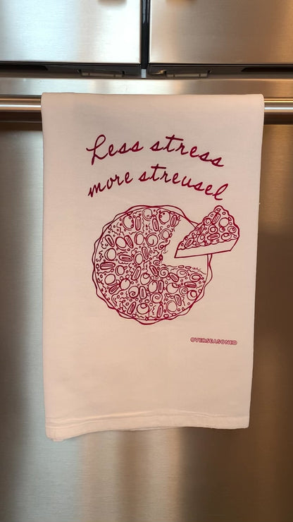 A white tea towel that reads "Less stress more streusel" hangs in a kitchen