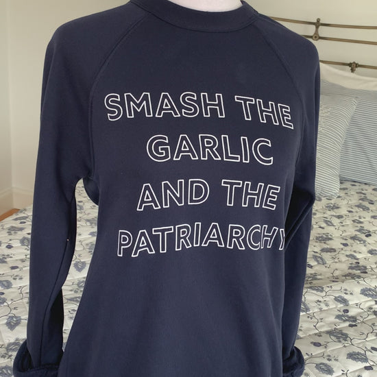 A navy blue crewneck that reads "Smash the Garlic and the Patriarchy" hangs on a manikin