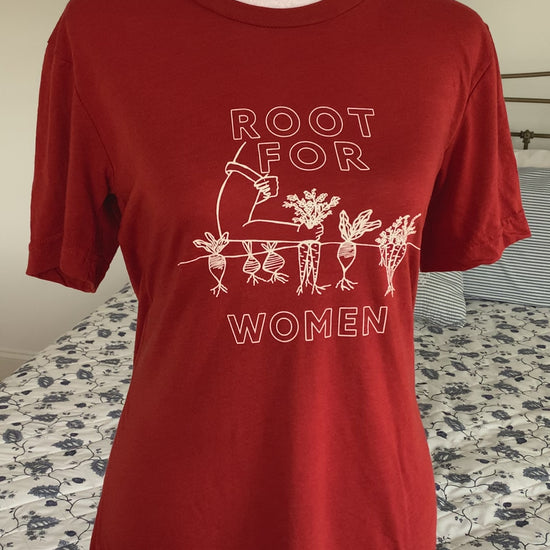 A red tee that reads "Root for Women" with a garden illustration hangs on a manikin