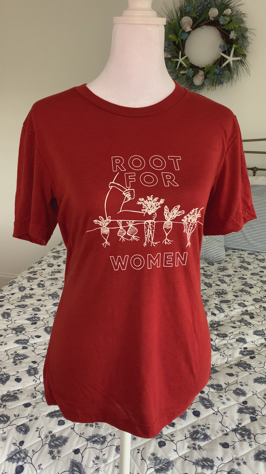 A red tee that reads "Root for Women" with a garden illustration hangs on a manikin