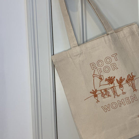 A canvas tote with the words "Root for Women" in orange block letters hangs on a doorknob