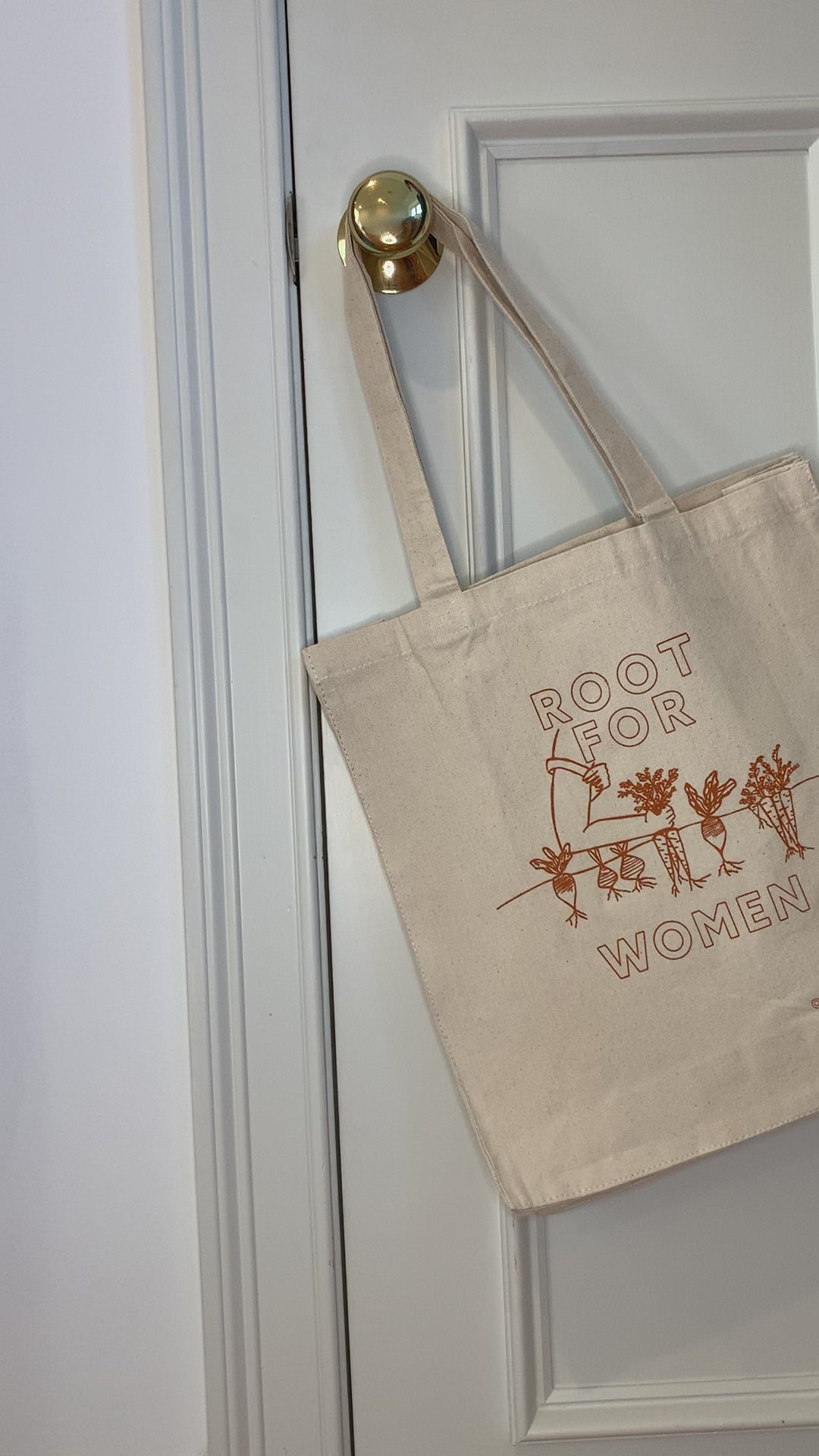 A canvas tote with the words "Root for Women" in orange block letters hangs on a doorknob