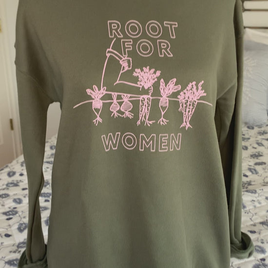 A green sweatshirt that reads "Root for Women" hangs on a manikin