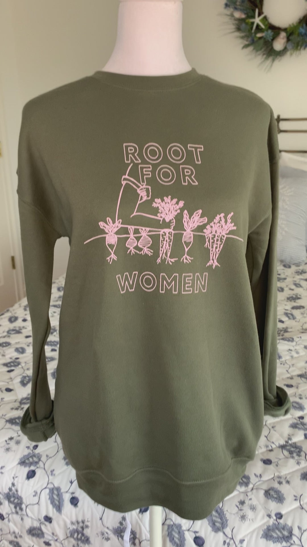 A green sweatshirt that reads "Root for Women" hangs on a manikin