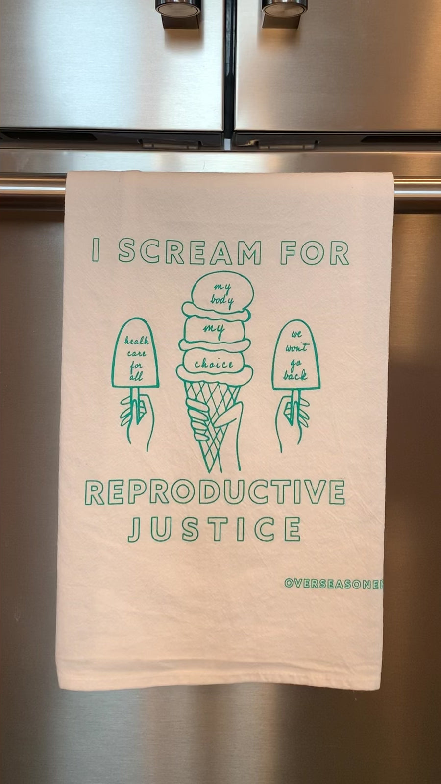 A white tea towel with mint green block letters that reads "I scream for reproductive justice" hangs in a kitchen