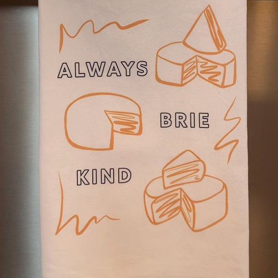 A tea towel hanging on a bar reads "Always Brie Kind"