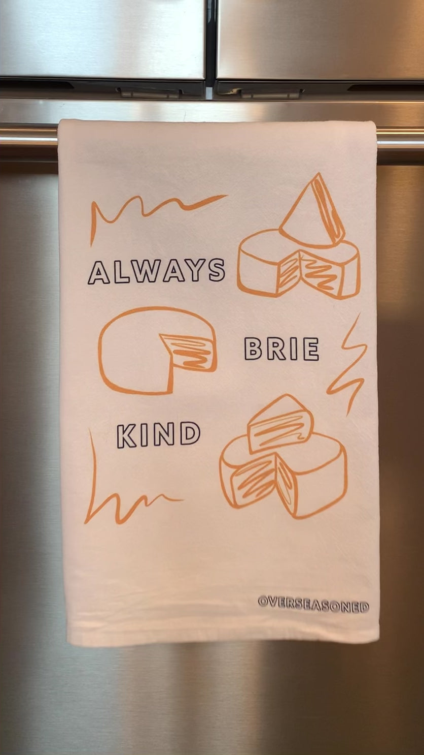 A tea towel hanging on a bar reads "Always Brie Kind"
