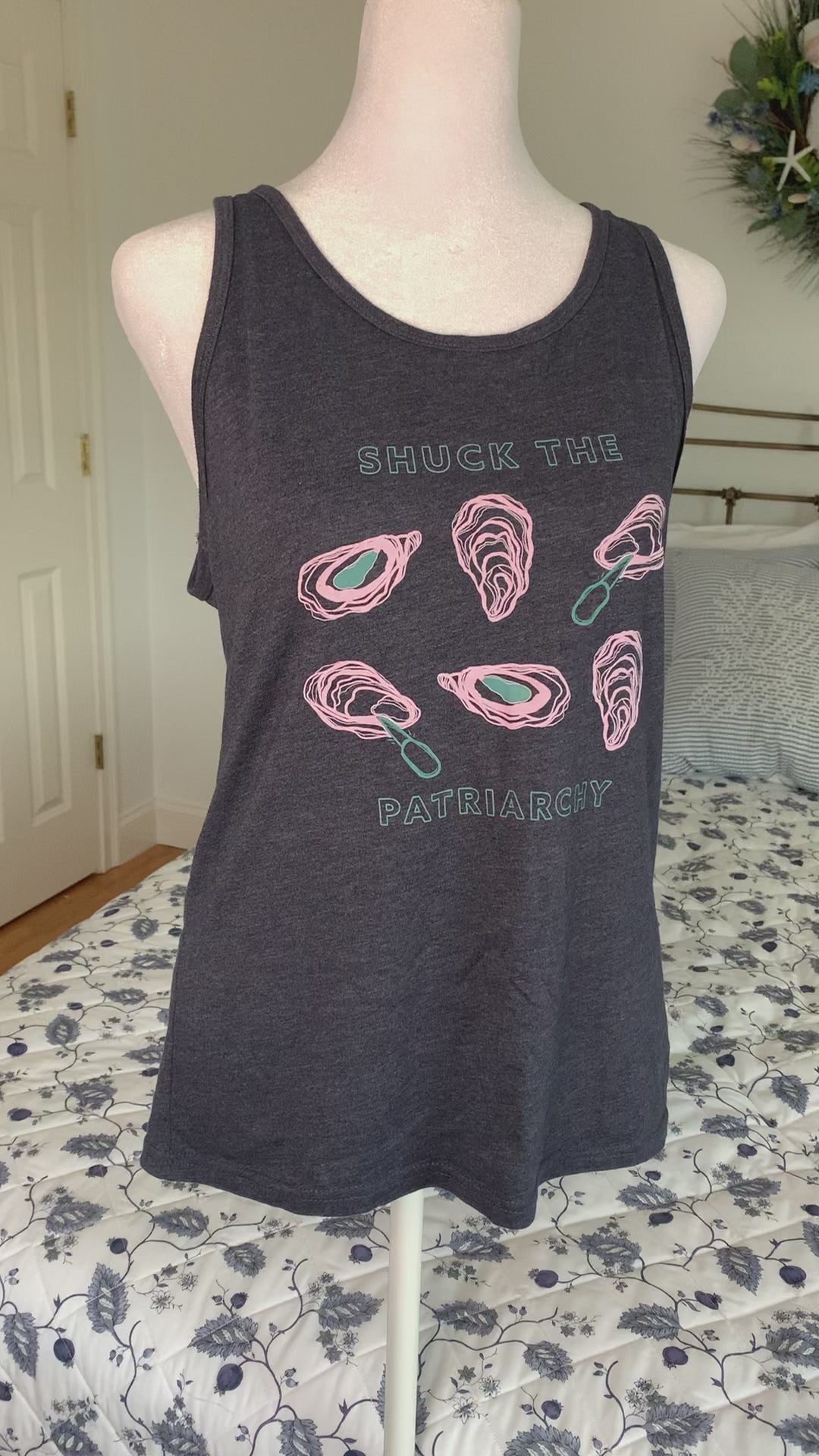 A heather navy tank that reads "Shuck the Patriarchy" hangs on a manikin