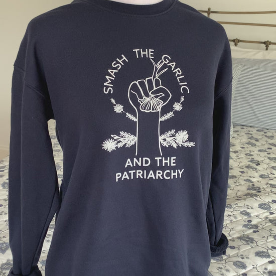 A navy crewneck that reads "Smash the Garlic and the Patriarchy" with a garlic illustration hangs on a manikin