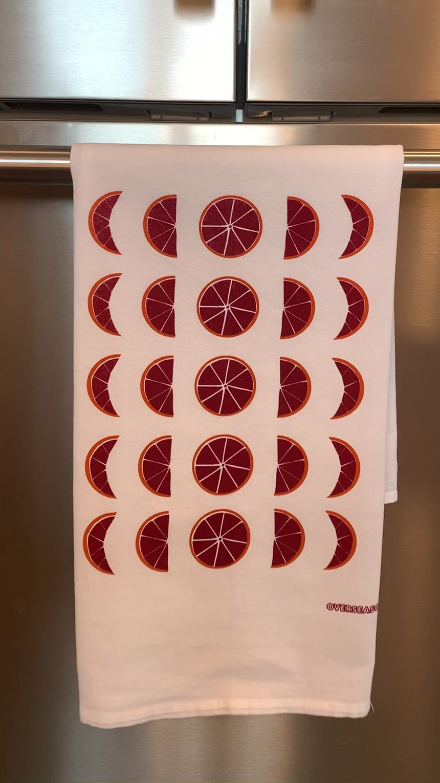 A white tea towel with blood orange moon designs hangs on a bar