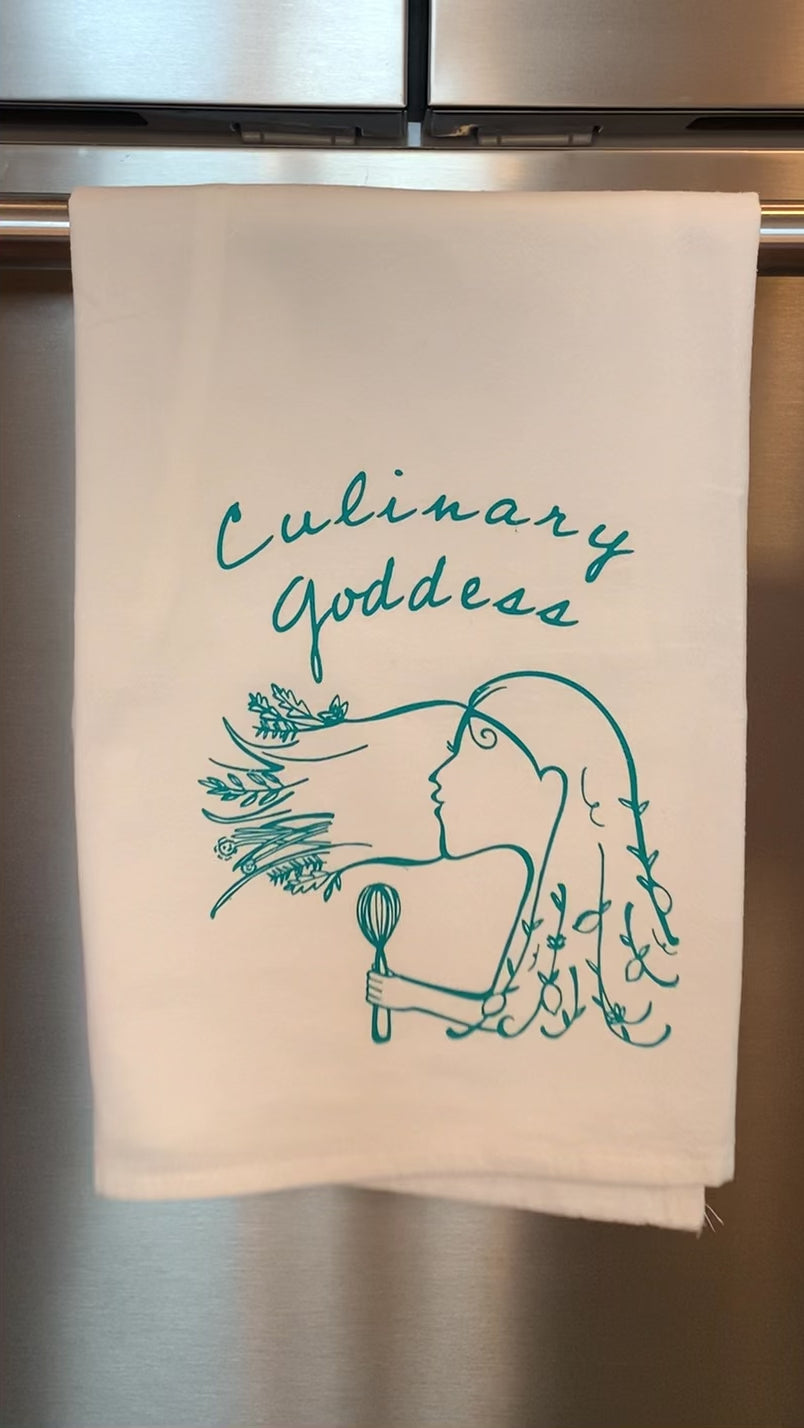 A white tea towel that reads "Culinary Goddess" in teal lettering hangs in a kitchen