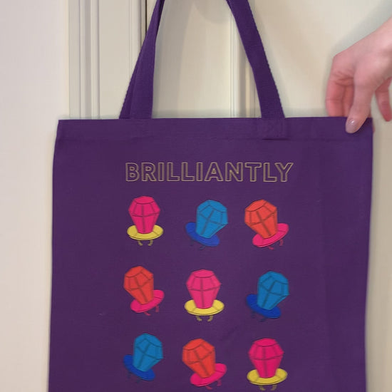 A purple tote that reads "Brilliantly Multifaceted" hangs from a doorknob