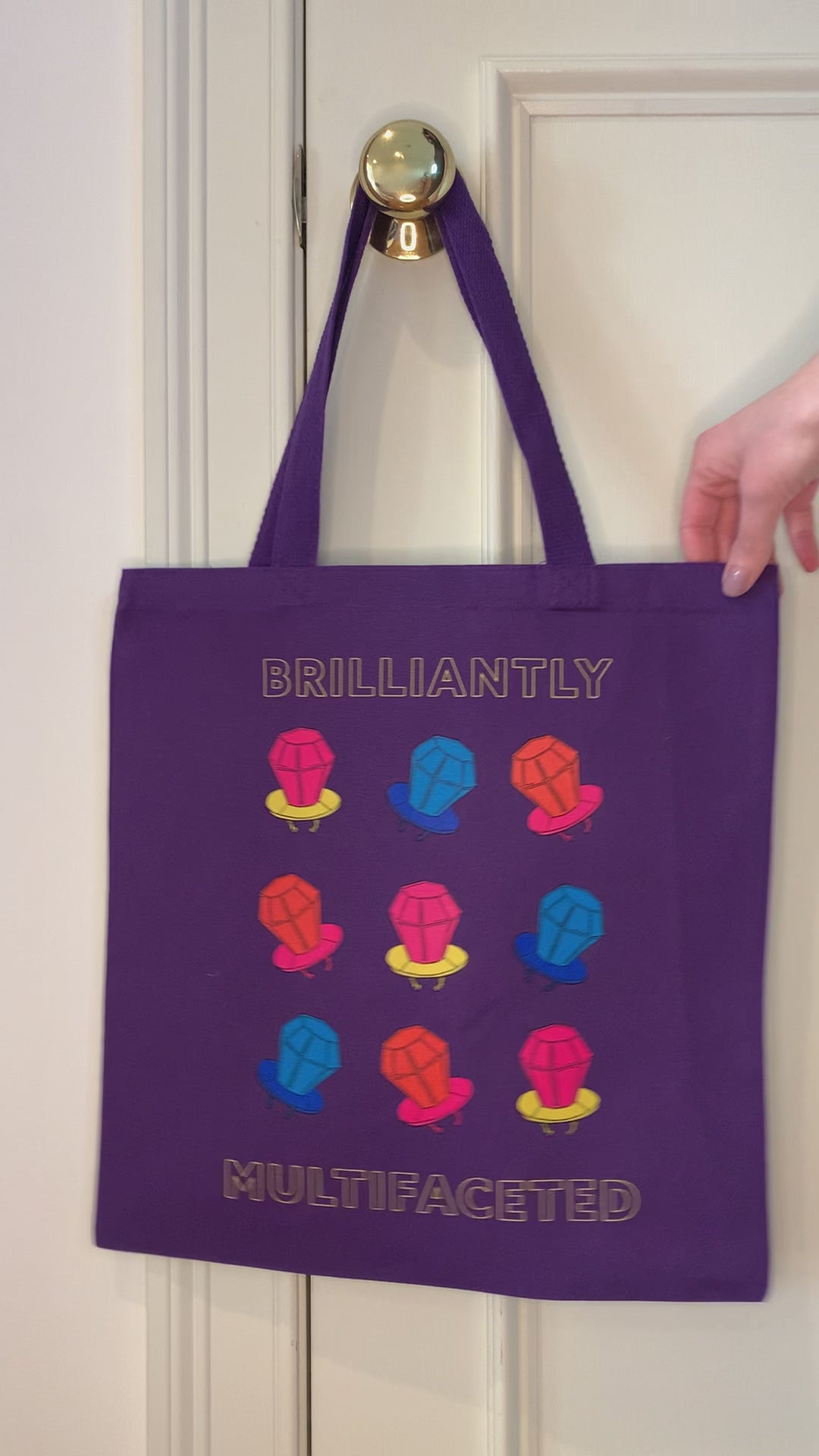 A purple tote that reads "Brilliantly Multifaceted" hangs from a doorknob