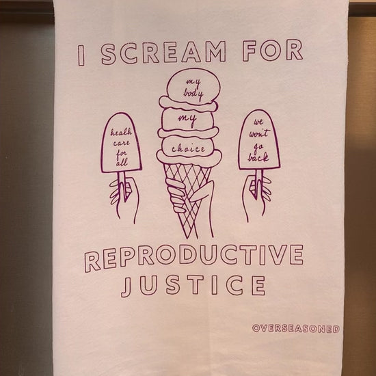 A white tea towel with raspberry block letters that reads "I scream for reproductive justice" hangs in a kitchen