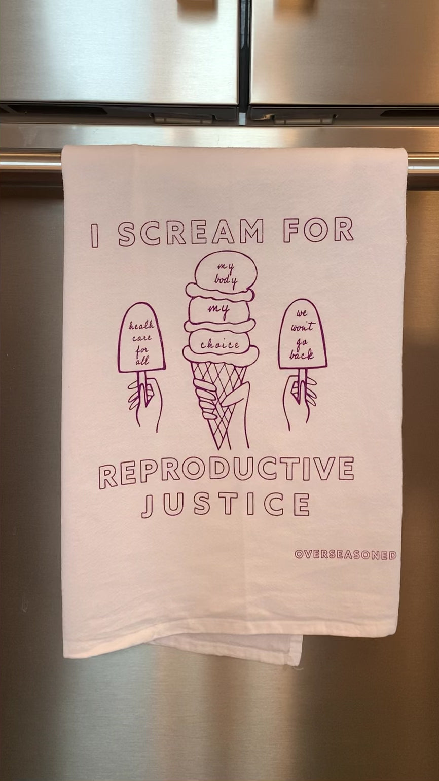 A white tea towel with raspberry block letters that reads "I scream for reproductive justice" hangs in a kitchen