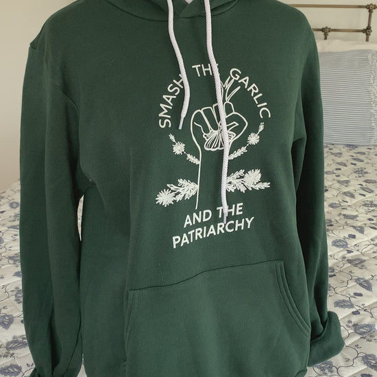A dark green hoodie that reads "Smash the Garlic and the Patriarchy" hangs on a manikin" 